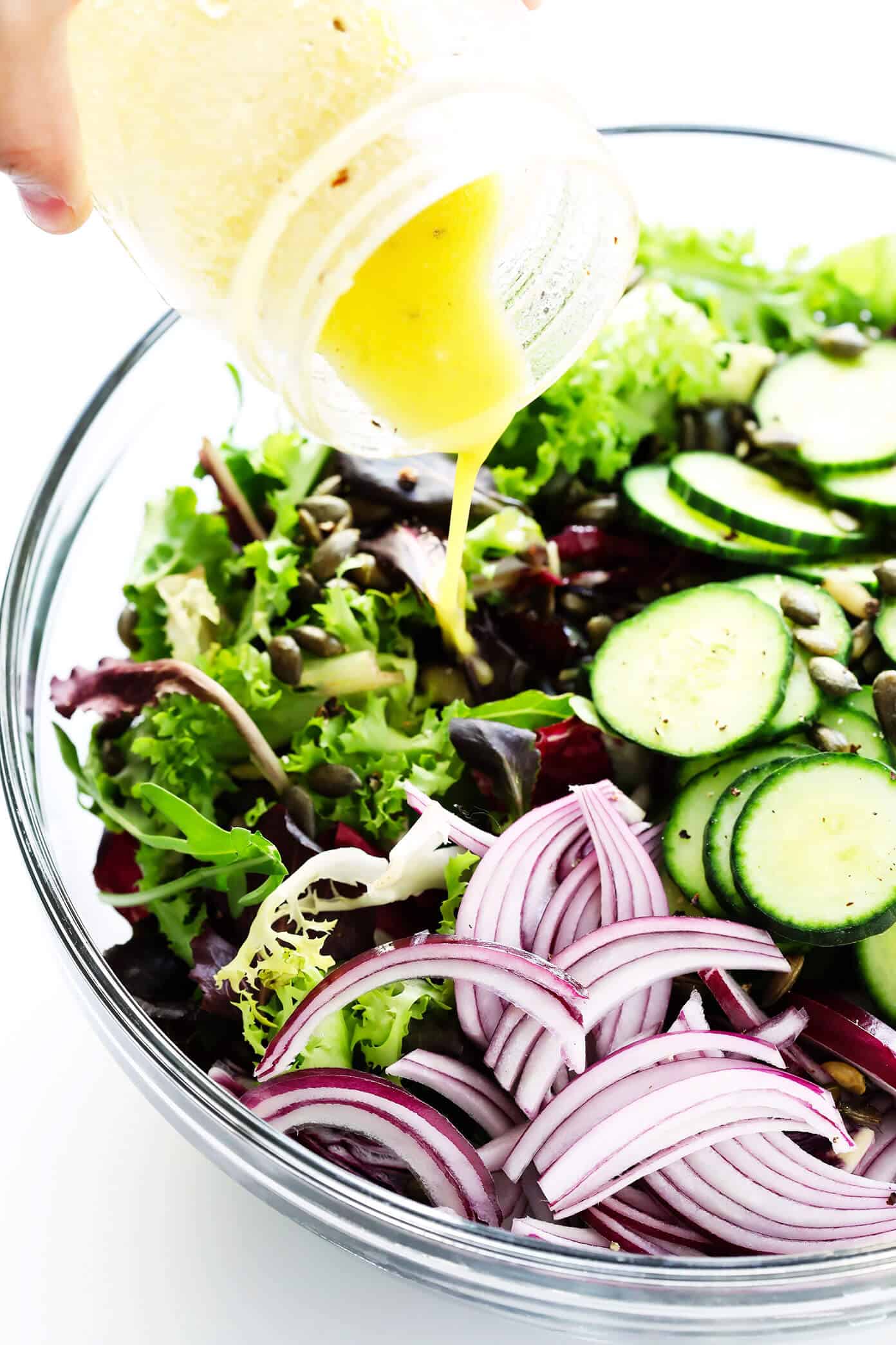 My favorite everyday salad recipe -- made with fresh greens, cucumber, red onion, pepitas (or your favorite nuts), and a simple lemon salad dressing. So easy, healthy and delicious! | gimmesomeoven.com #healthy #salad #recipe #dinner #vegetarian #vegan #glutenfree #easy #dressing #vinagirette Adding salad dressing to salad bowl