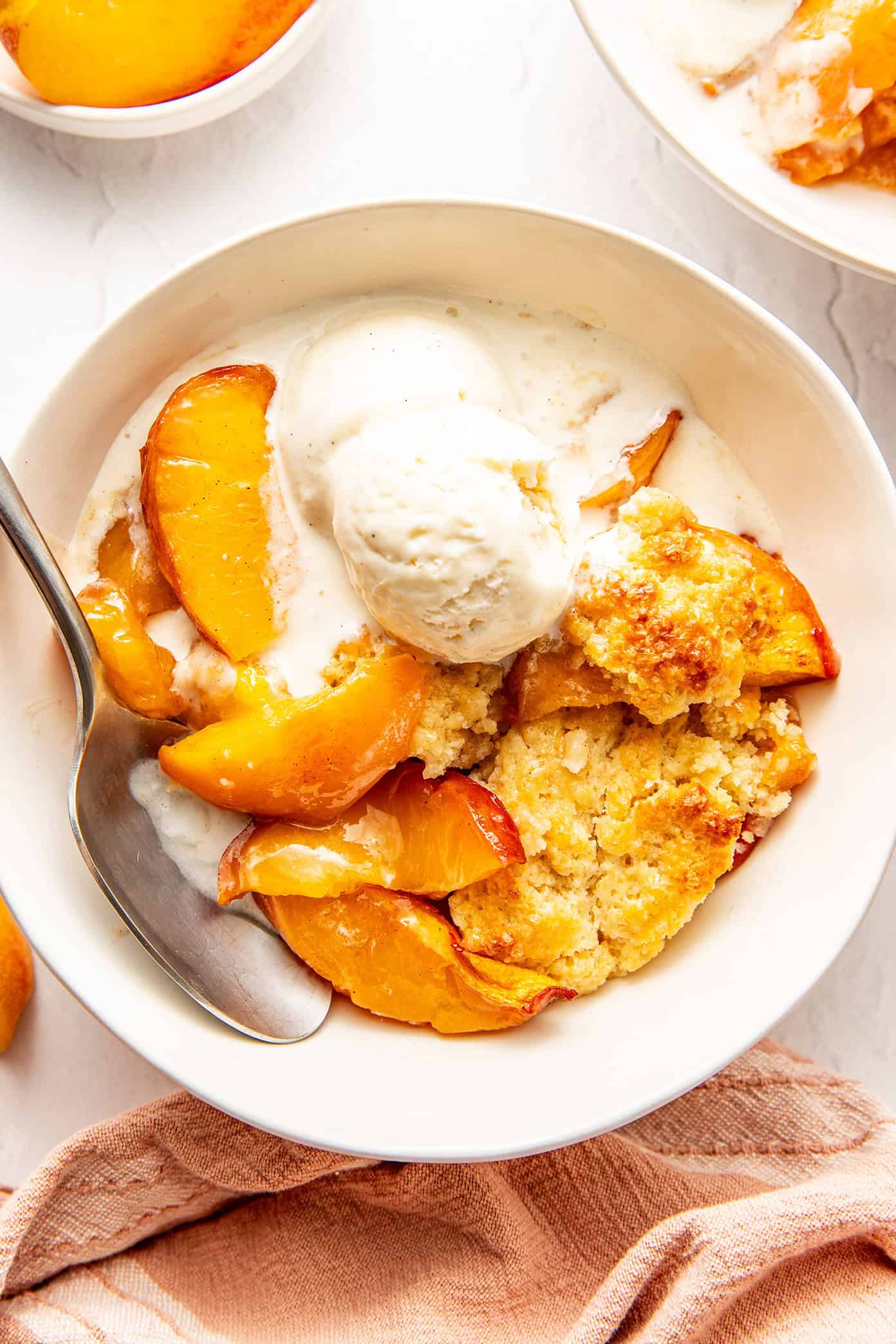 fresh peach cobbler in a bowl with melty vanilla ice cream